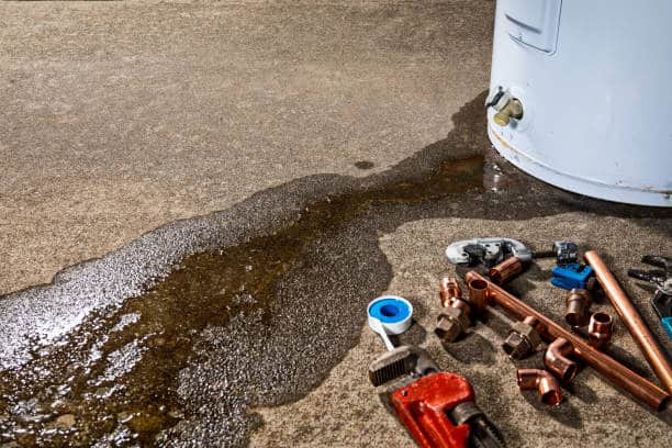 Water leaks near a boiler, copper pipes, and a wrench on a concrete floor.