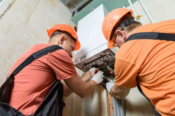 Two technicians repair heating equipment in the basement of a building.