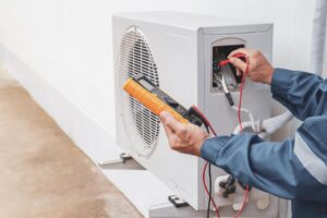 HVAC technician in blue jacket tests outdoor AC unit using special tool