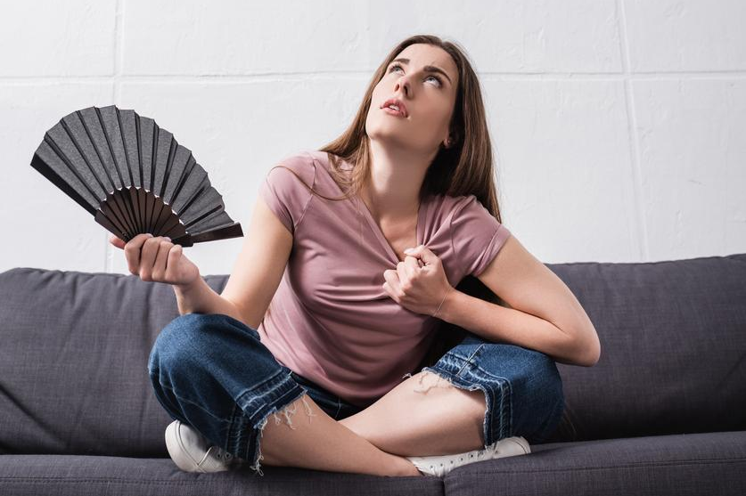 Woman sits on couch fanning herself as she tries to cool off