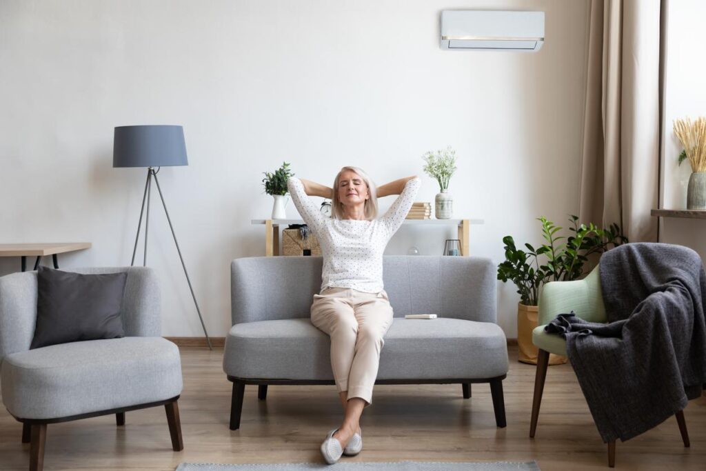 An older woman relaxing at home with a wall-mounted air conditioner in the background