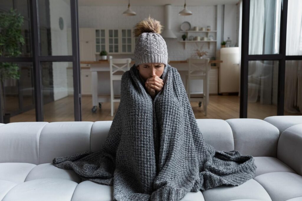 A young woman shivering at home with a broken furnace.