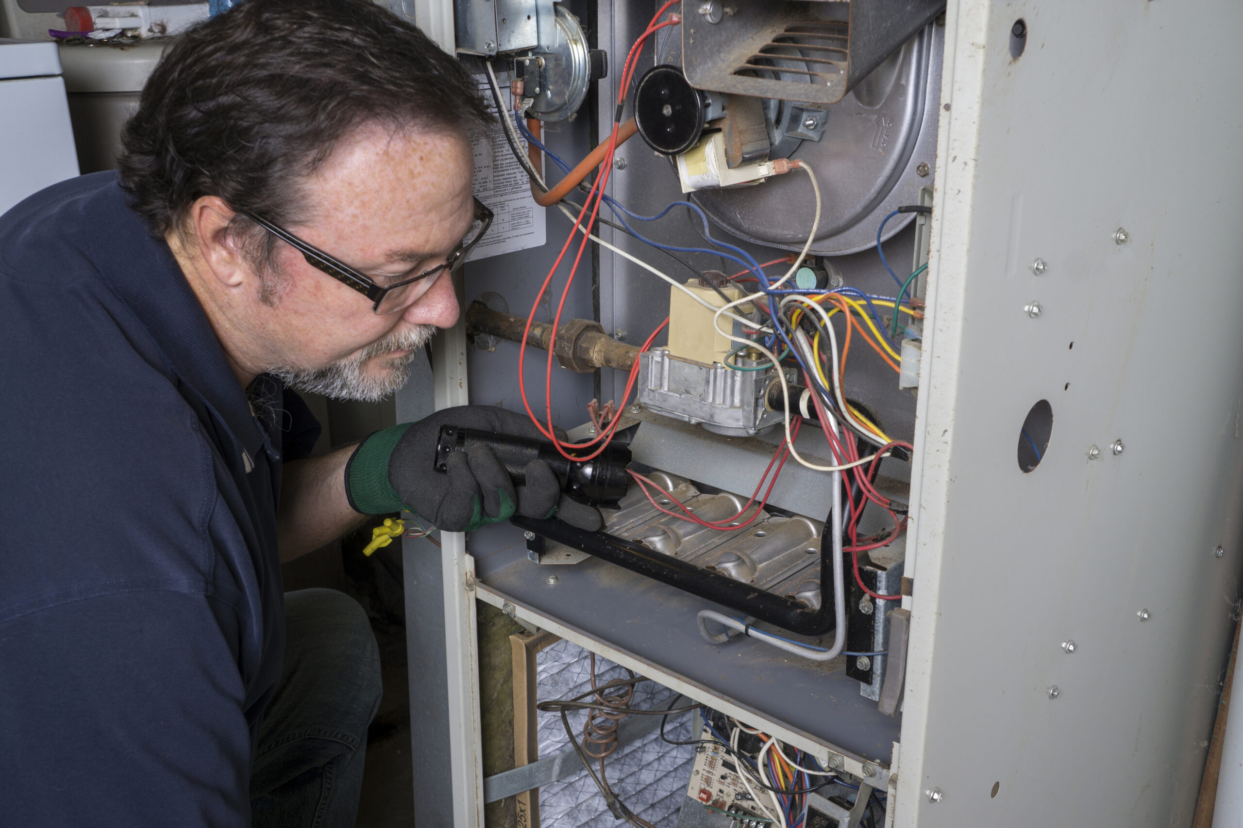 Technician looking over a gas furnace with a flashlight